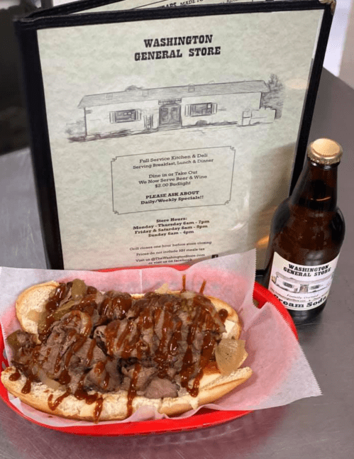 A sandwich filled with beef, peppers, and barbecue sauce, served in a basket with a menu and a bottle of soda in the background.
