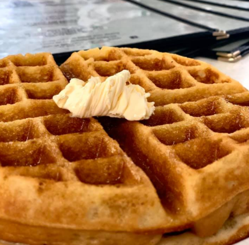 A golden waffle topped with a pat of butter, placed on a table with menus in the background.