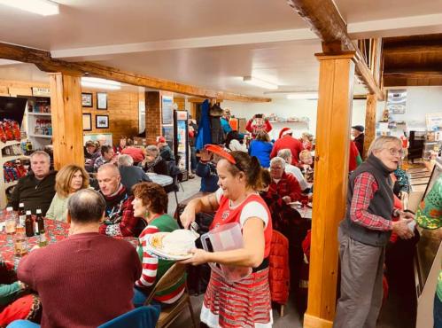 A festive gathering with people in holiday attire, enjoying food and drinks in a cozy, decorated space.