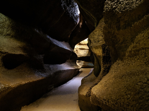 A narrow, winding cave with textured rock walls and soft lighting illuminating the path ahead.