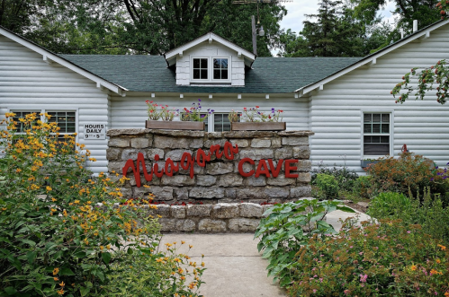 Entrance to Niagara Cave, featuring a stone sign and colorful flowers in a lush garden setting.