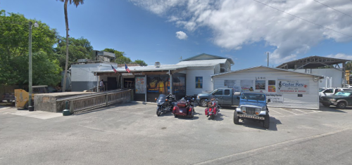 A rustic building with a sign, featuring parked motorcycles and a truck in front, under a partly cloudy sky.