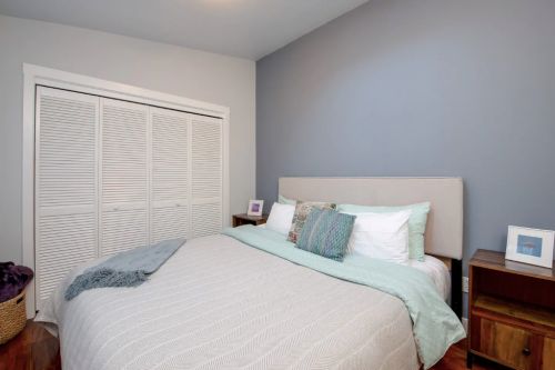 Cozy bedroom with a light gray wall, a bed with teal and white bedding, and a closet with sliding doors.