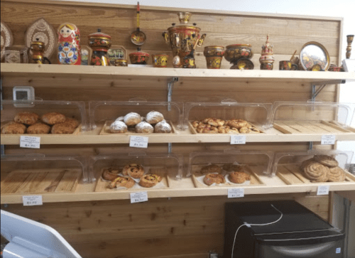 A wooden shelf displays various baked goods and colorful decorative items, including matryoshka dolls and pottery.
