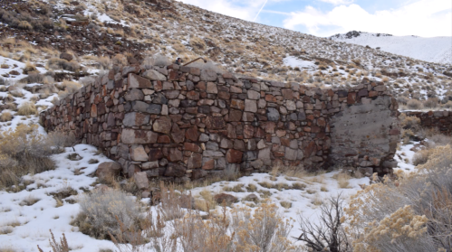 Abandoned stone structure in a snowy, mountainous landscape with sparse vegetation.