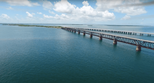 Aerial view of a long bridge extending over calm blue waters under a partly cloudy sky.