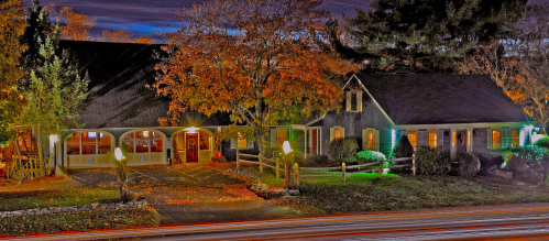 A charming house at night, surrounded by autumn foliage and softly lit by streetlights, with a winding driveway.