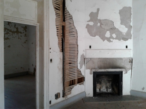 An empty room with peeling paint, exposed walls, and a fireplace, showcasing signs of neglect and disrepair.