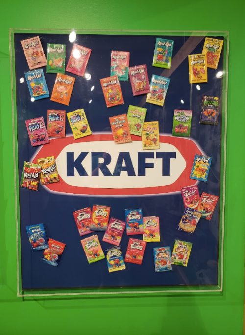A colorful display of various Kool-Aid packets arranged around the Kraft logo on a green background.