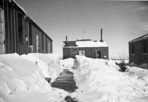 Snow-covered pathway between buildings, with deep snowdrifts and clear blue sky above.