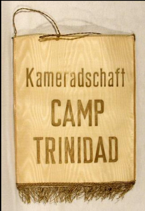 A decorative banner reading "Kameradschaft CAMP TRINIDAD" with a fringed bottom and a hanging cord.