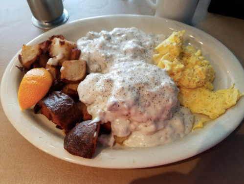 A plate of biscuits and gravy, scrambled eggs, and seasoned potatoes, garnished with an orange slice.