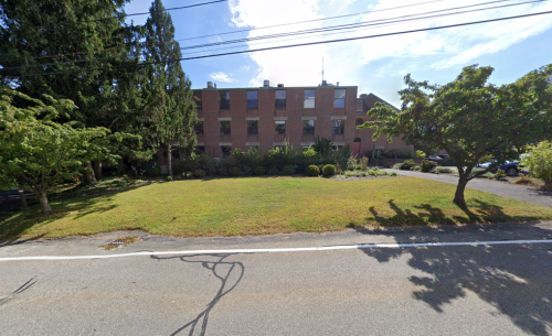 A brick building surrounded by greenery and trees, with a clear blue sky overhead.