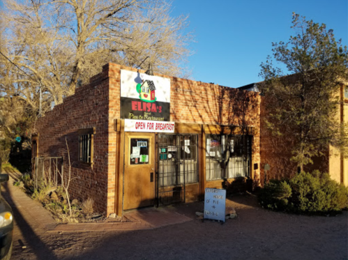 A brick building with a sign reading "Elisa's" and "Open for Breakfast," surrounded by trees and shrubs.