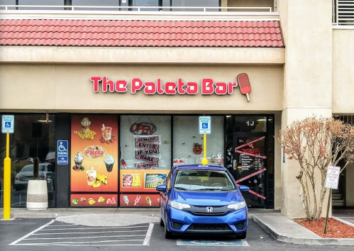Exterior of The Poleta Bar with a blue car parked in front, featuring colorful signage and an open sign.