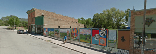 A street view of a small town with colorful murals on a fence and a person walking nearby.