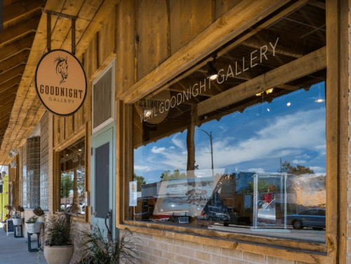 Exterior view of Goodnight Gallery, featuring a sign and reflections in the window, with a rustic wooden facade.