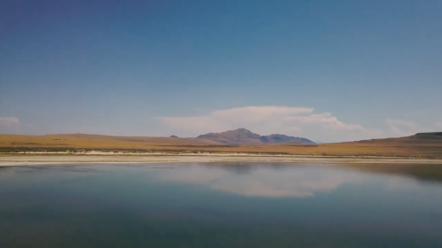 A serene landscape featuring a calm lake reflecting mountains and a clear blue sky.