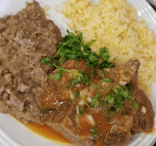 A plate featuring rice, refried beans, and a piece of meat topped with tomato sauce and fresh cilantro.