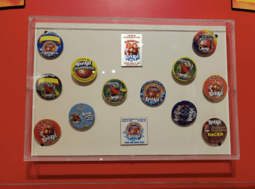 A display case featuring various colorful Kool-Aid drink mix packets arranged in a grid pattern.