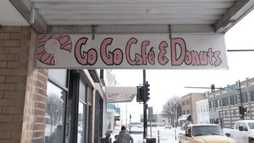 Sign for "Go Go Café & Donuts" with a pink donut graphic, located on a snowy street.