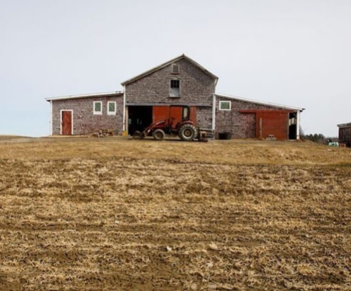 A rustic farm with a red tractor parked in front of a weathered barn on a barren landscape.