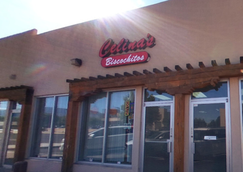 Sign for "Celina's Biscochitos" on a storefront with large windows and wooden accents. Sunlight shines in the background.
