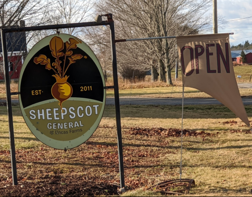 Sign for Sheepscot General at Uncas Farms, established 2011, with an "OPEN" flag nearby.