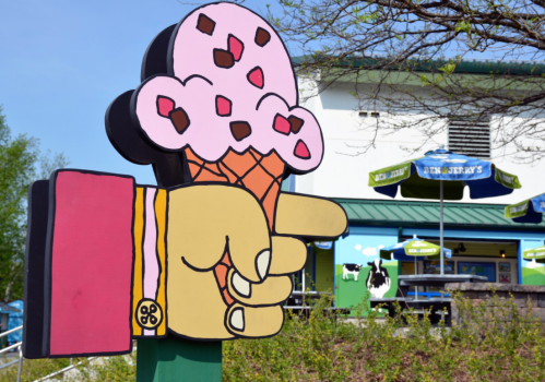 A colorful sign featuring a hand holding an ice cream cone with pink ice cream and chocolate chunks.