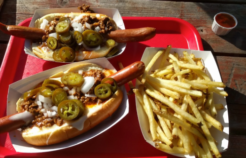 Two loaded hot dogs topped with chili, onions, and jalapeños, served with a side of crispy French fries.