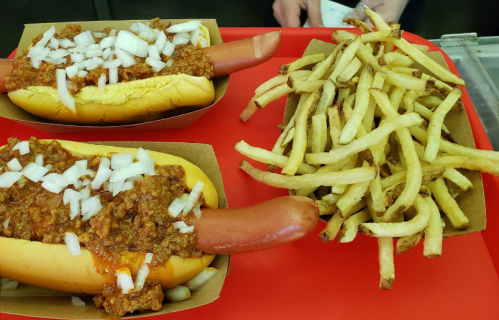 Two chili dogs topped with chopped onions on a red tray, accompanied by a serving of crispy French fries.