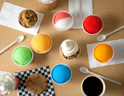 A variety of colorful ice cream cups arranged on a table, with spoons and napkins nearby.
