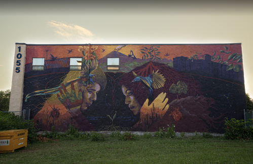 A vibrant mural on a building depicting two faces surrounded by nature and colorful elements, showcasing artistic expression.