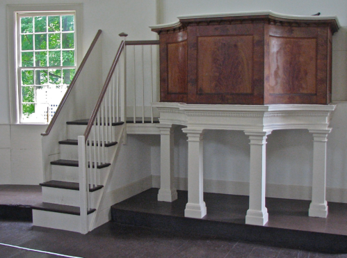 Interior of a room featuring a wooden pulpit on a raised platform and a staircase leading up to it.