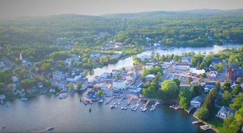 Aerial view of a picturesque lakeside town surrounded by lush greenery and boats docked along the shore.