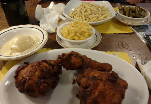 A plate of fried chicken with sides of macaroni and cheese, green beans, and mashed potatoes on a wooden table.