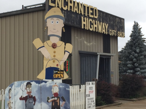A whimsical gift shop with a large cartoon figure outside, featuring a sign that says "You're Open" and colorful artwork.