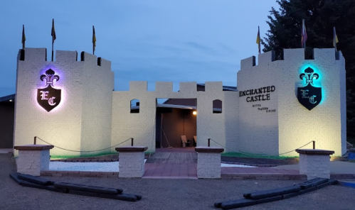 Entrance to Enchanted Castle, featuring a stone wall with flags and illuminated shields, set against a twilight sky.