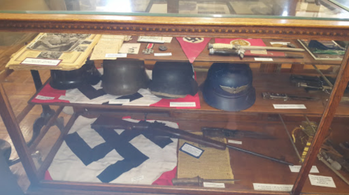 Display case featuring historical military artifacts, including helmets, flags, and weapons from a past era.
