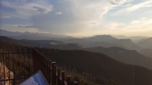 A scenic view of mountains and valleys under a cloudy sky, with a fence in the foreground.
