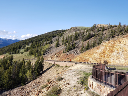 A winding road along a hillside with trees and rocky terrain under a clear blue sky.