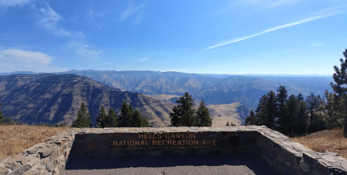 View of Hell's Canyon National Recreation Area with mountains and clear blue sky in the background. Stone overlook in foreground.