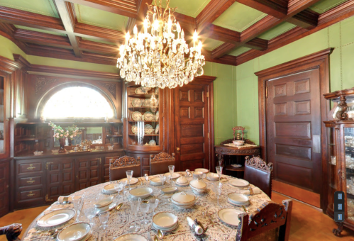 Elegant dining room with a chandelier, ornate wooden furniture, and a beautifully set table.