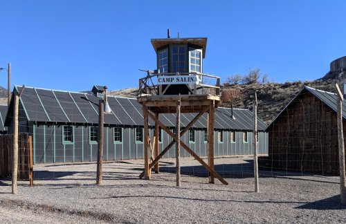 A historic camp with a watchtower labeled "Camp Salina" and surrounding buildings against a clear blue sky.