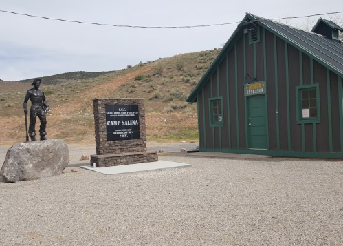 A rustic building with a green door and a statue of a soldier in front, marking the entrance to Camp Salina.