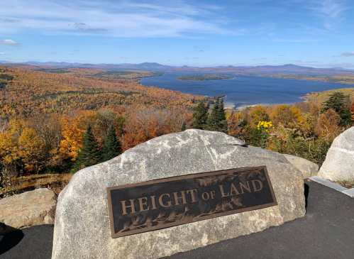 A scenic view from Height of Land, showcasing vibrant autumn foliage and a lake under a clear blue sky.