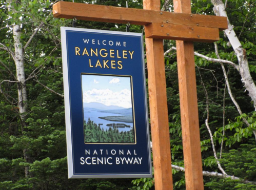 Sign welcoming visitors to Rangeley Lakes, featuring a scenic view of lakes and trees, with "National Scenic Byway" below.