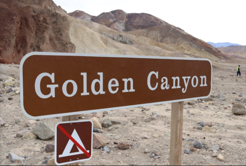 Sign for Golden Canyon in a rocky, desert landscape with mountains in the background.