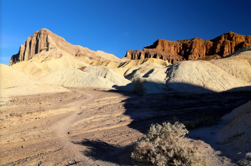 A rugged landscape featuring colorful hills and a prominent peak under a clear blue sky.