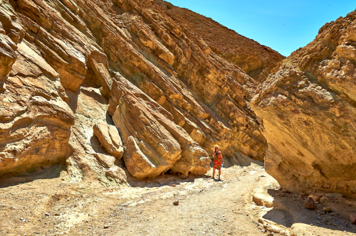 A person in a red dress stands among large rock formations in a desert landscape under a clear blue sky.